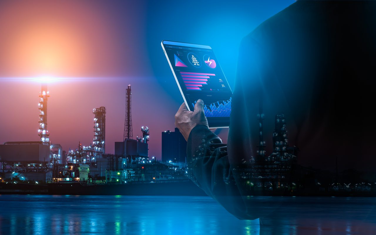 Engineer reviewing inspection data on a tablet in front of a refinery at night